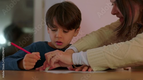 Frustrated mother assisting young son with homework at table correcting mistake and guiding learning during challenging homeschooling session at home