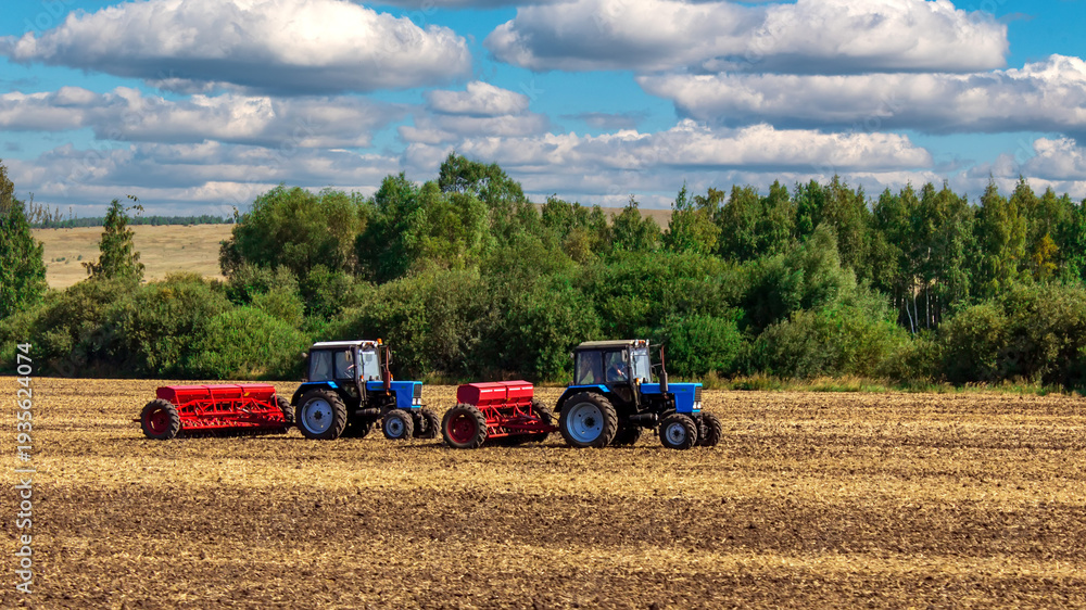 Fototapeta premium Two tractors are doing sowing or harvesting in the field.