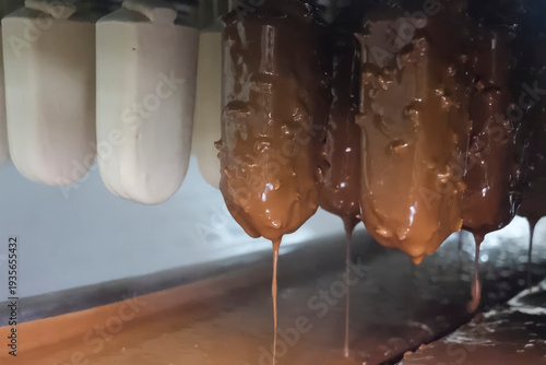 Ice cream on stick, dipped in chocolate glaze with nuts, a mass conveyor of ice cream production at the factory.