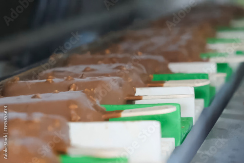 Ice cream on stick, dipped in chocolate glaze with nuts, a mass conveyor of ice cream production at the factory.