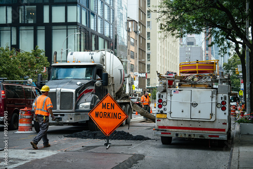 Фотография Construction workers in safety vests operate near a cement truck on an urban street