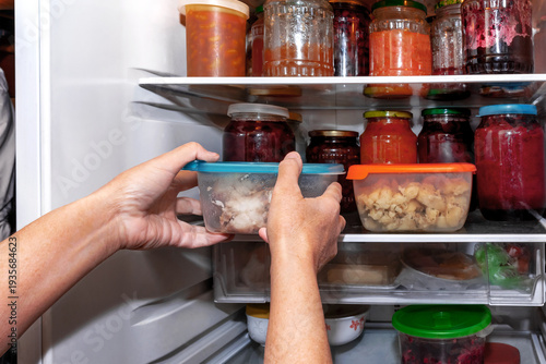 A housewife puts packaged food into a household refrigerator.