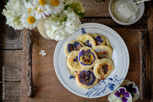 Gourmet flower pancakes served with sour cream on a rustic wooden table.