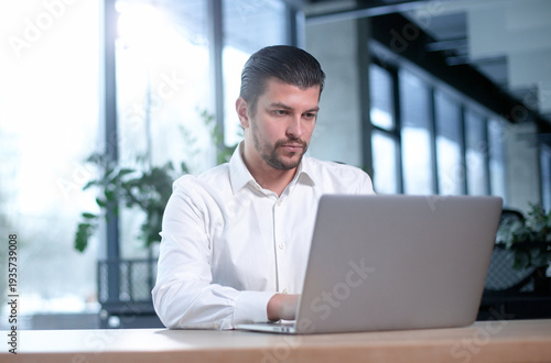 A man is sitting at a desk with a laptop in front of him