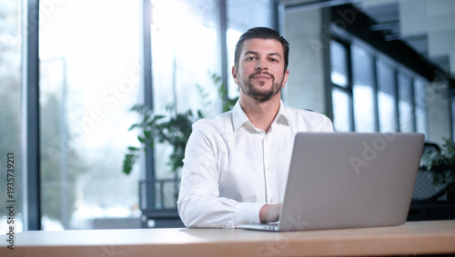 A man is sitting at a desk with a laptop in front of him