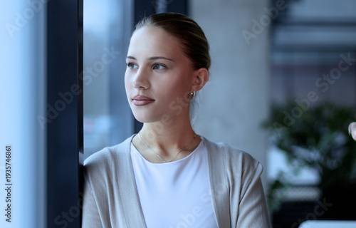 A woman is standing in front of a window with her hand on her chin
