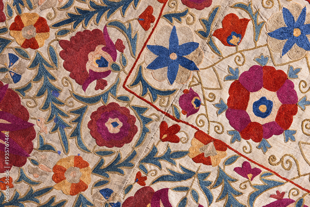 Fototapeta premium Intricate colorful wall embroidery on a traditional textile featuring hand-stitched Uzbek floral motifs, swirling vines and ornamental patterns. Close-up detail highlights texture and craftsmanship