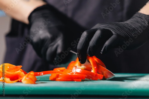 Картината върху платно Chef slicing red bell peppers with black gloves on green cutting board