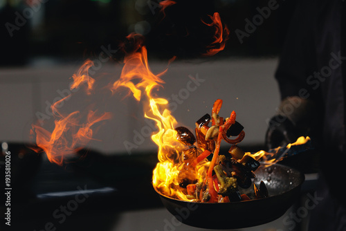 Foto Dramatic stir fry flames in kitchen with vegetables on fire, man chef prepares f