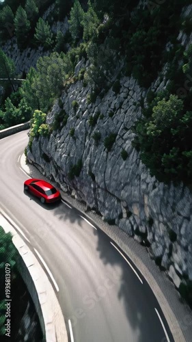 Red car navigates a winding mountain road through lush green trees