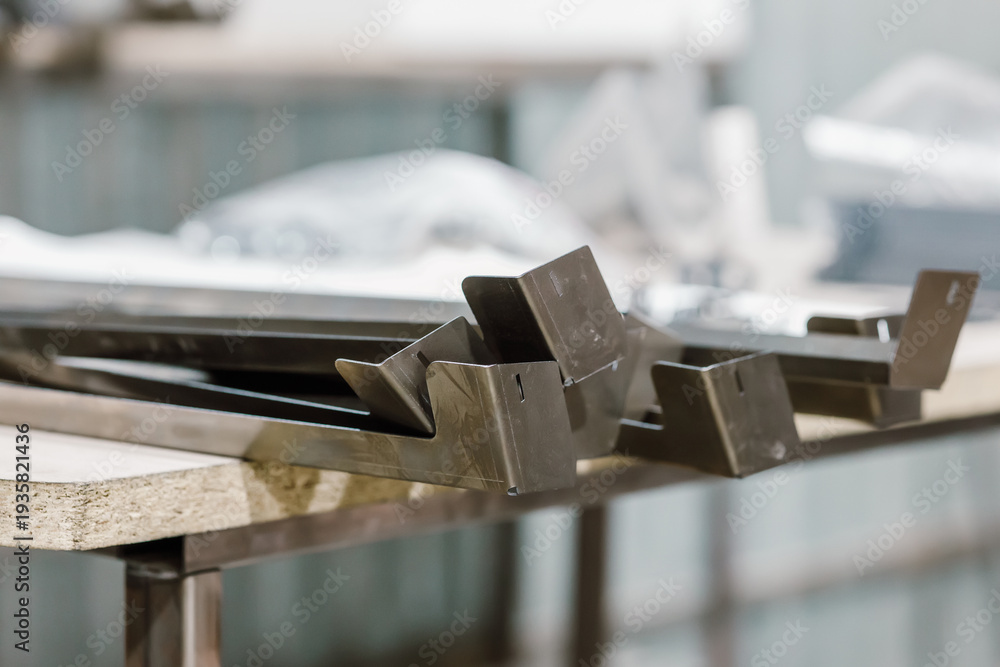 Obraz premium Finished metal parts and bent steel components on a workbench in a manufacturing workshop.