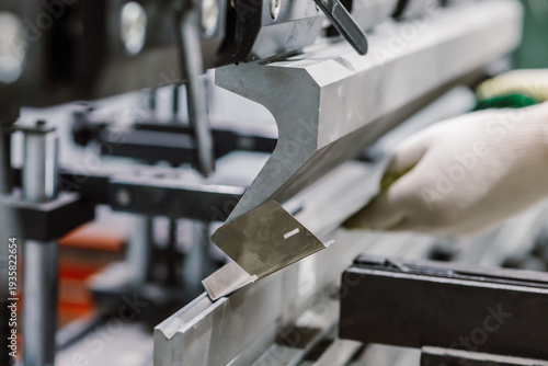 Close up of worker hands in gloves using hydraulic press brake for metal sheet bending.