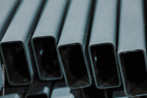 Close up of rectangular metal pipes and steel profiles with grey coating in industrial workshop.