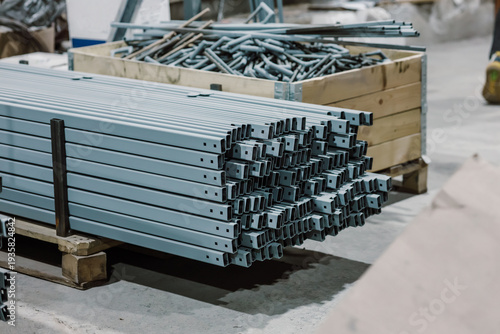 Finished metal profiles and steel brackets stacked on wooden pallets in a factory warehouse.