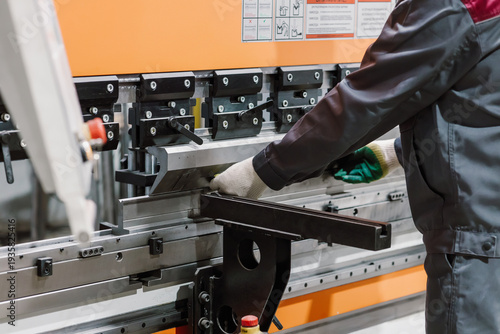Close up of worker hands in gloves using hydraulic press brake for precision metal sheet bending.