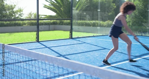 Woman lunging, retrieving ball near net after paddle-swing, readying shot on blue court, copy space