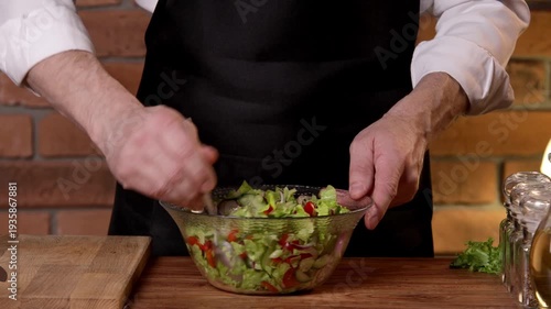 A male chef mixes a salad and slices black olives.