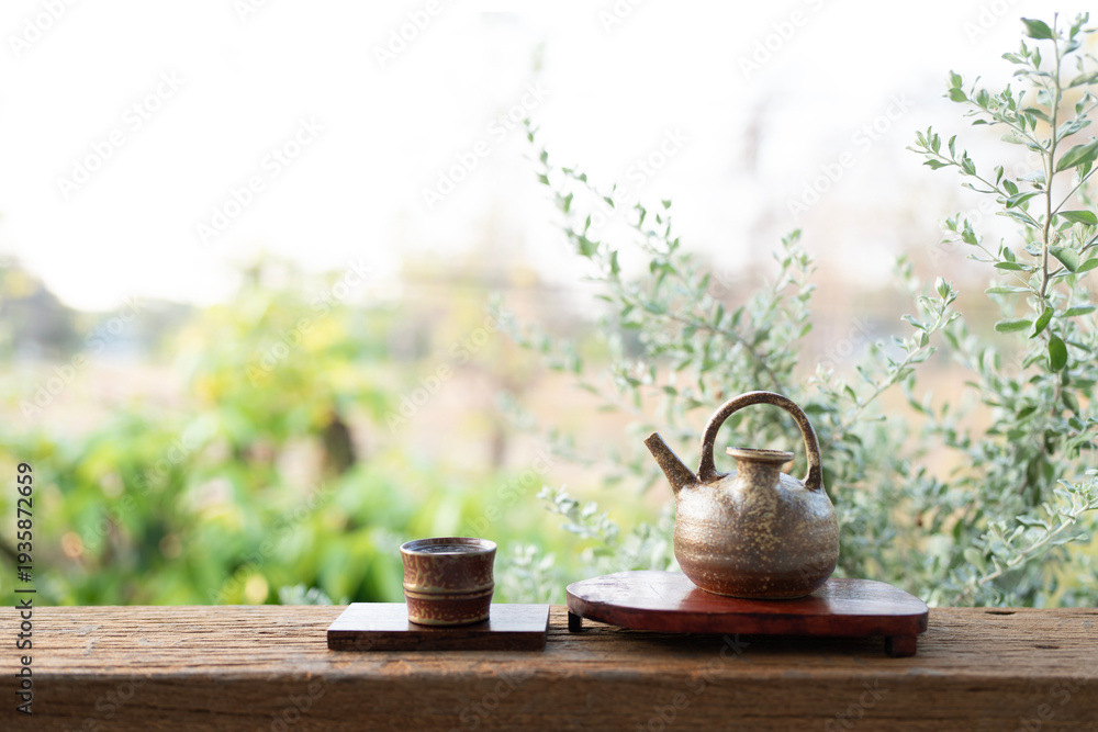 Fototapeta premium Ancient rustic teapot and cup on wooden table with outdoor view