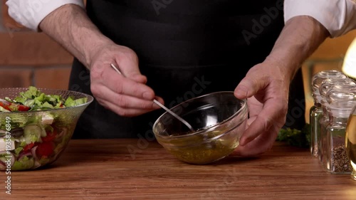 A male chef stirs salad dressing with olive oil in a cup.