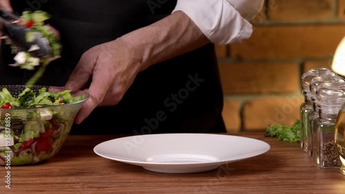 A male chef serves salad from a bowl onto a white plate.