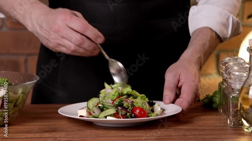 A male chef mixes a salad on a white plate and adds vegetable oil dressing.