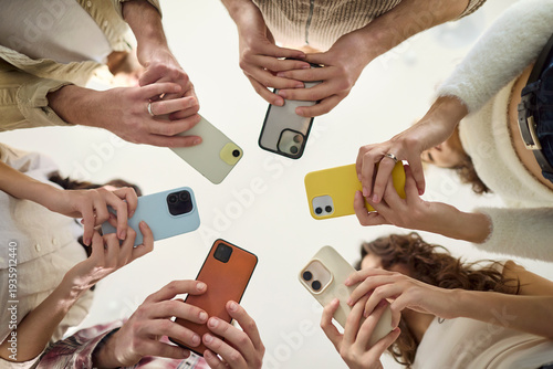 People in a circle use smartphone phones together. A diverse group shares screens to boost communication, social links, and network during a meeting. Clear concept of connected teamwork.