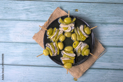 Fotografie Traditional Spanish gilda skewers with olives, anchovies and peppers on a blue w