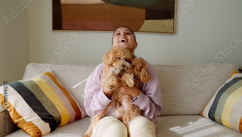 Woman lifts playful poodle with sunshine and bright cushions
