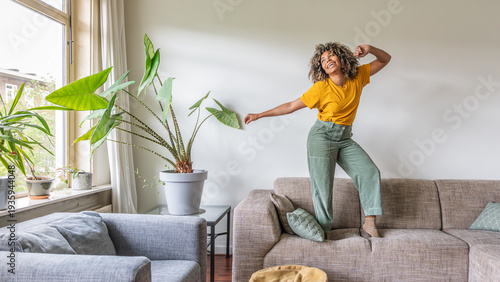 Happy afro american woman dancing on the sofa at home - Smiling girl enjoying day off lying on the couch - Healthy life style, good vibes people and new home concept