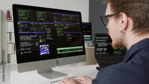 Over shoulder shot of young adult male computer programmer with glasses typing on keyboard debugging system or application errors while working at office desk