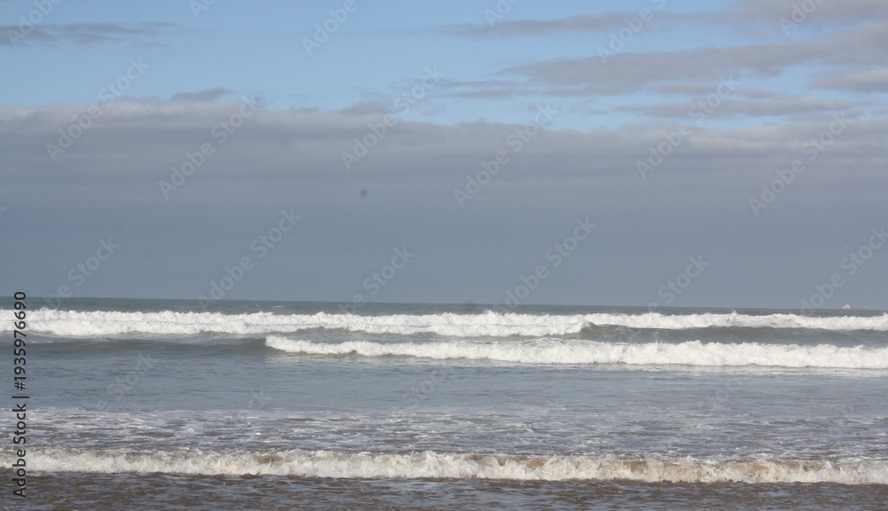 Obraz premium Agadir beach on the Atlantic coast with blue waves and golden sand, Agadir Oufella rising on the hill in the distance under bright sunlight, scenic panoramic view. Photo taken Feb 18, 2026.