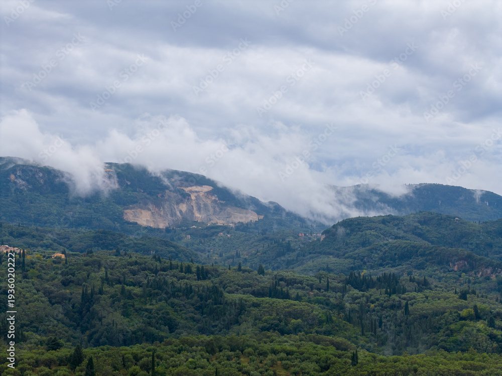 Obraz premium Greek island landscape with vast olive groves and a large mountain quarry. Misty clouds cover hills in rural Corfu, Greece
