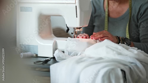 Female tailor sewing fabric in sewing machine. Female worker sewing white wedding dress with machine. DIY process of sewing at home workshop project