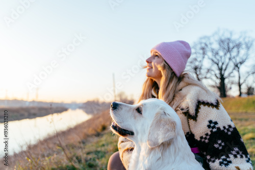 Smiling female, blonde Caucasian, sharing upward gaze with golden retriever at sunset