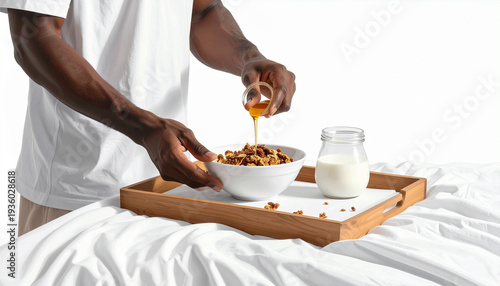 Dark-skinned man pours honey over granola cereal breakfast served on wooden tray in bed with milk jar early morning