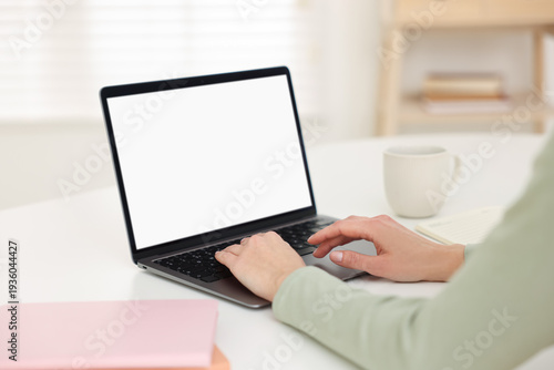 Woman working on laptop at white table indoors, closeup