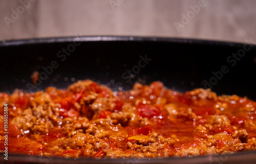 Close-up of minced beef simmering in rich tomato sauce, creating a hearty homemade bolognese. Hot, flavorful meat sauce bubbling in a pan during the cooking process.