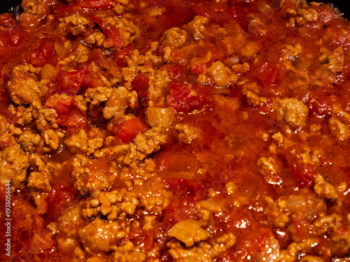 Close-up of minced beef simmering in rich tomato sauce, creating a hearty homemade bolognese. Hot, flavorful meat sauce bubbling in a pan during the cooking process.