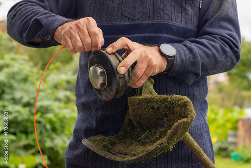Man installing new trimmer line on a grass trimmer head. Garden maintenance and home improvement concept for outdoor work. close up view