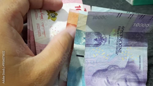 a person holding a stack of Indonesian Rupiah banknotes  The visual of cash money can symbolize various financial themes such as salary, savings, profit, expenses, inflation