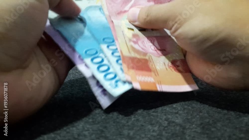 a person counting Indonesian Rupiah banknotes, illustrating concepts related to finance, economy, business transactions, income management, and daily life