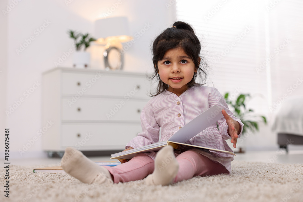 Naklejka premium Cute little girl reading book on floor at home. Space for text