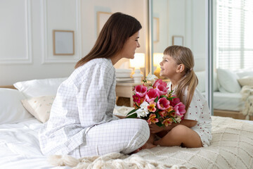 Happy Mother's Day. Mom and her daughter with bouquet of beautiful flowers on bed at home