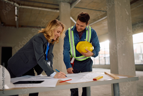 Happy architect and construction site worker going through housing plans during home remodeling project.