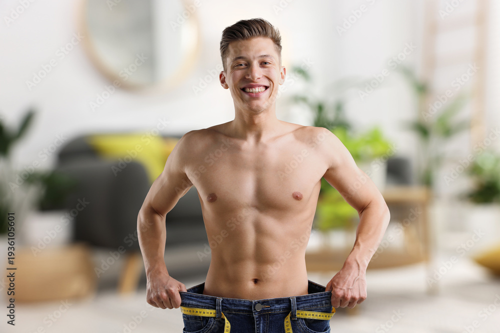 Fototapeta premium Happy man in his old jeans showing weight loss result at home