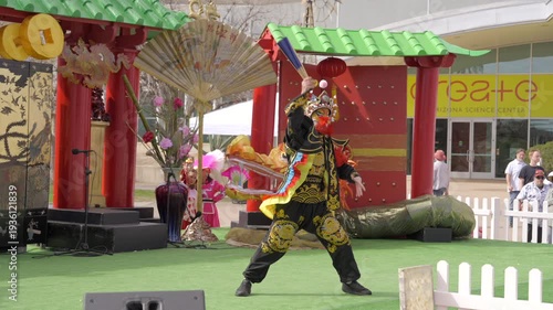 This slow motion video shows a traditional face changing Chinese dancer performing on an outdoor stage. 