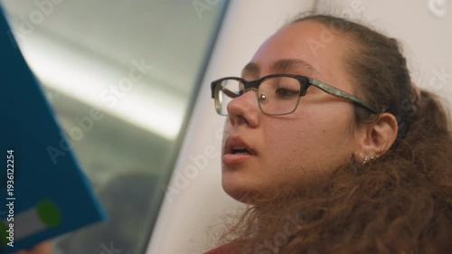 Lady reads aloud. Passenger softly recites on train. Focused female traveler narrates during railway journey. Woman with curly hair concentrates and recites words quietly on moving train