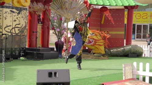 This video shows a traditional face changing Chinese dancer leaping and twirling their fan in slow motion on an outdoor stage. 