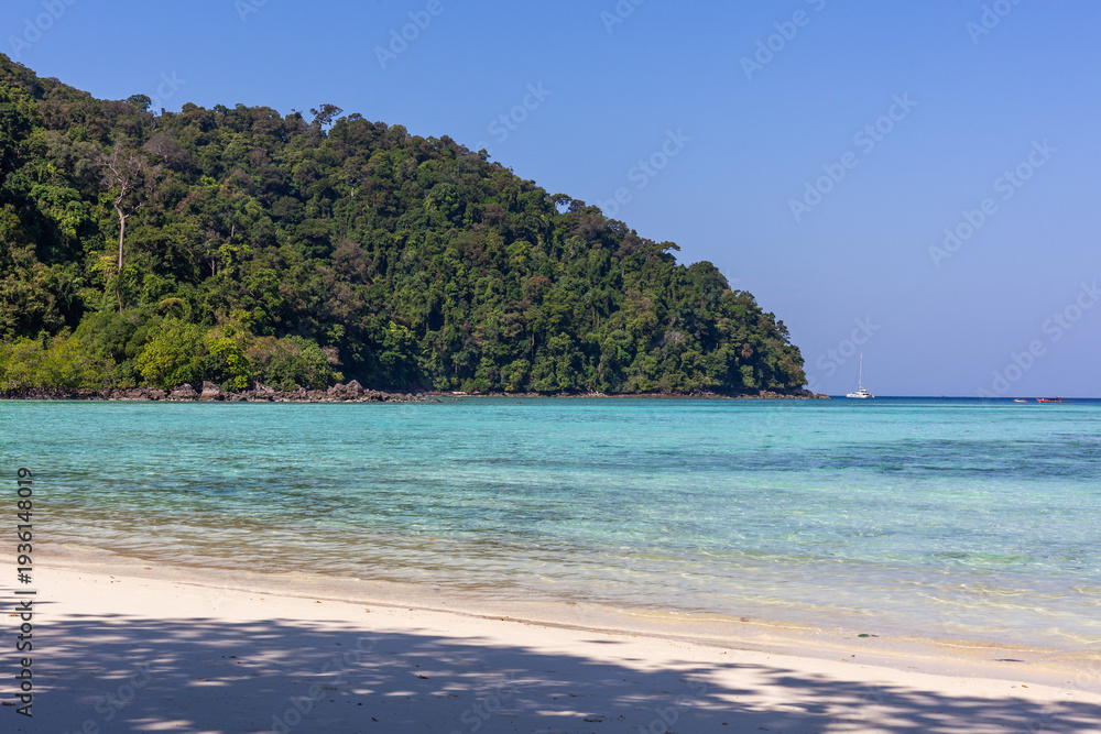 Obraz premium Tropical beach at Koh Surin, Thailand. Clear turquoise water and sandy shore. Lush green hillside in the background. Calm and serene coastal setting.