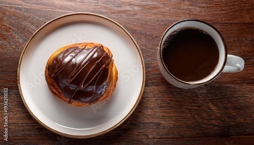 chocolate drizzled pastry on a plate beside a cup of coffee on a wooden table